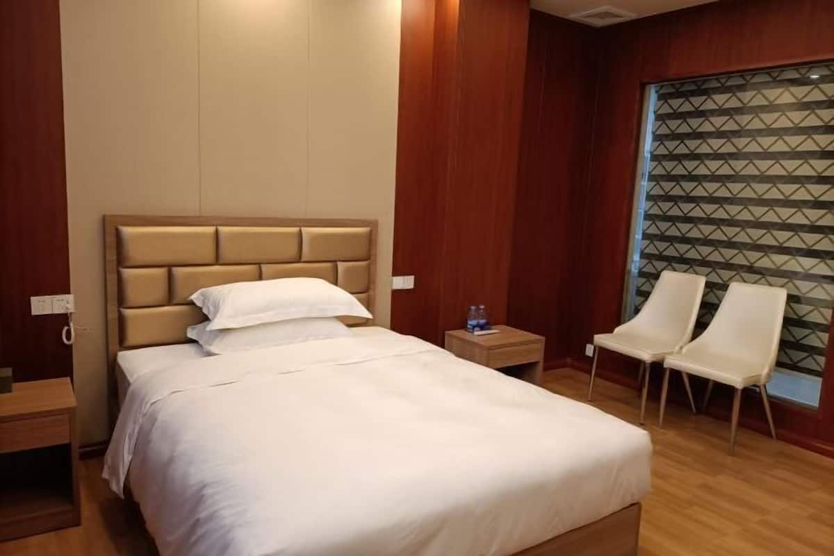 A hotel room with a bed, bedside table, two chairs, and a window with a geometric pattern.