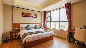 A hotel room with a large bed, a desk, a chair, a window with curtains, and a painting on the wall.