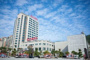 A multi-story hotel with a prominent red sign, a parking lot with several vehicles, and a clear blue sky. - Lian Shan Longshan Garden Hotel (Lianshan)