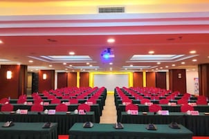 Un salón de conferencias con filas de mesas, sillas y un escenario al frente.