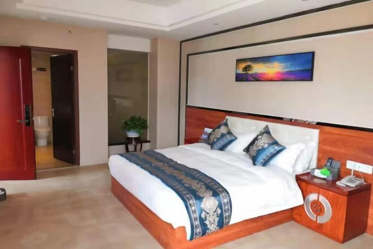 A hotel room with a large bed, a wooden headboard, a bedside table with a phone, and a painting on the wall.
