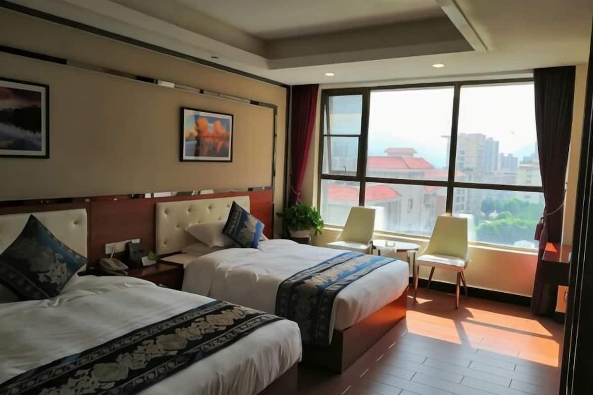 A hotel room with two beds, a large window with a city view, a small table, and a chair.