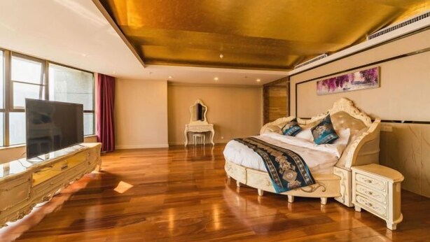 A bedroom with a large bed, a dresser, a vanity, and a television. - Lian Shan Longshan Garden Hotel (Lianshan)