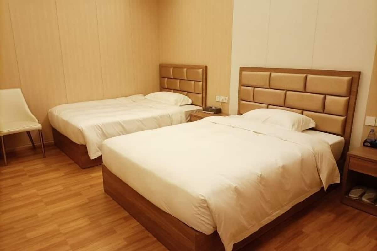 A hotel room with two beds, a chair, and a wooden floor.
