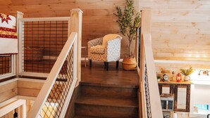 Un interior de madera con una escalera, un sillón estampado y una planta en maceta.
