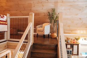 A wooden interior with a staircase, a patterned armchair, and a potted plant.