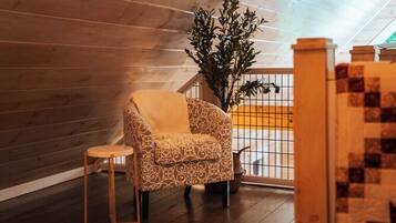 A cozy room with a patterned armchair, a small wooden stool, and a potted plant.