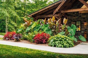 A building with a stone facade and wooden beams, surrounded by a variety of large, leafy plants.