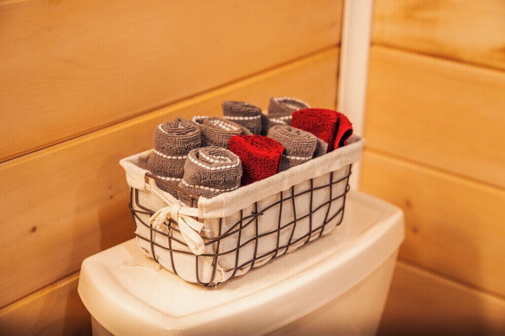 A white toilet with a wire basket containing rolled towels.