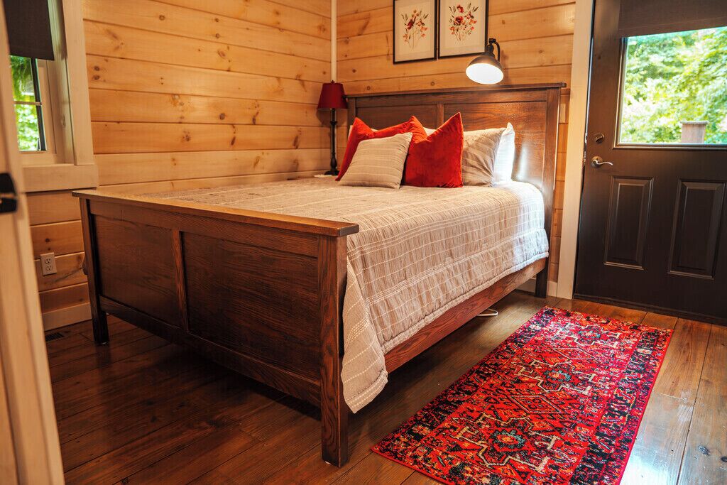 A wooden-paneled room with a bed, a red rug, and a door with a window.