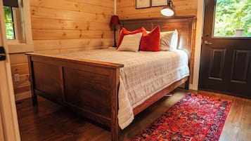 A wooden-paneled room with a bed, a red rug, and a door with a window.