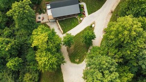 Vista aérea de una casa rodeada de abundante vegetación, con un camino de entrada pavimentado.