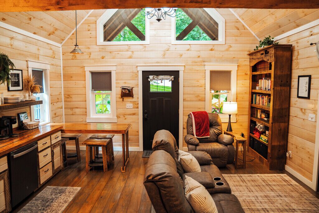 A cozy cabin interior with a wooden interior, a dining area, a sofa, and a bookshelf.