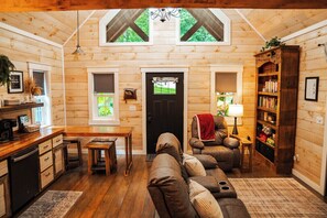 A cozy cabin interior with a wooden interior, a dining area, a sofa, and a bookshelf.