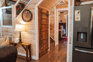 Een houten interieur met een klok, een deur, een tafel met een lamp en een koelkast.