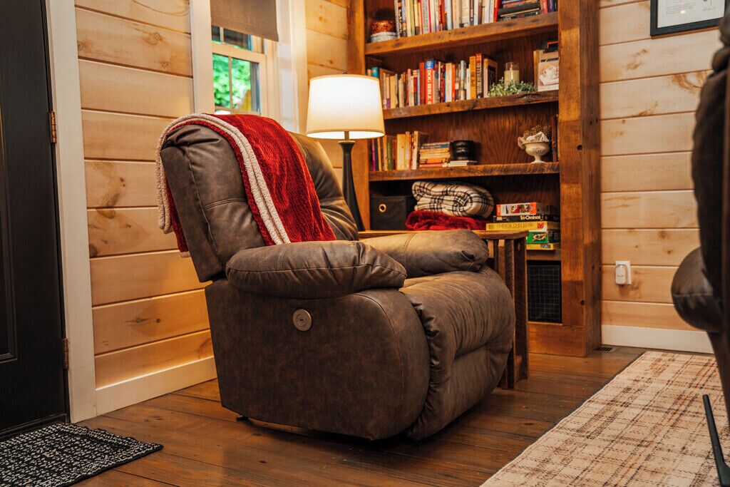 A cozy room with a leather recliner, a bookshelf, and a lamp.