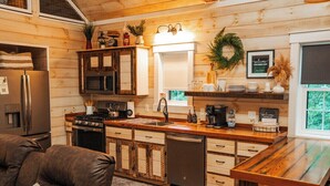 Un interior de madera con una zona de cocina, que incluye un refrigerador, estufa y microondas. Hay una mesa de comedor de madera y un sofá con cojín.