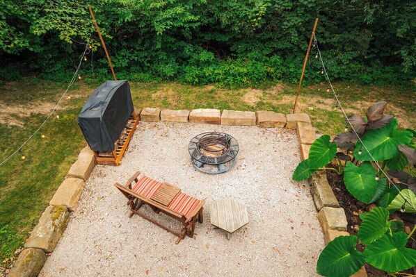 A backyard with a fire pit, a covered grill, a wooden bench, and a small table.