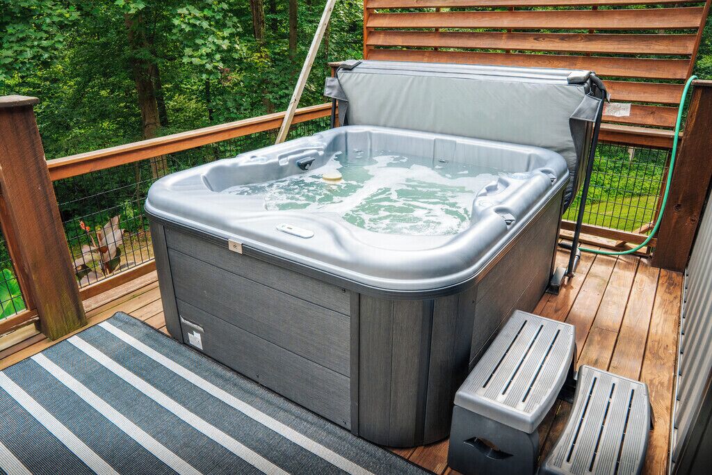 A hot tub on a wooden deck with a metal railing and a wooden fence in the background.