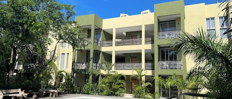 Un hotel de varios pisos con piscina, mobiliario exterior y abundante vegetación.