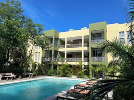 A multi-story hotel with a swimming pool, outdoor seating, and lush greenery.
