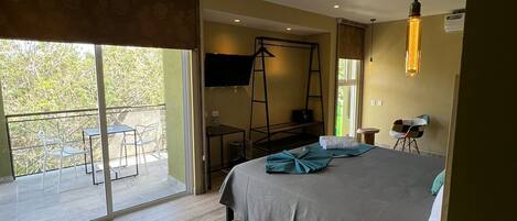 A modern bedroom with a large bed, a TV, a ladder, and a balcony with outdoor seating.