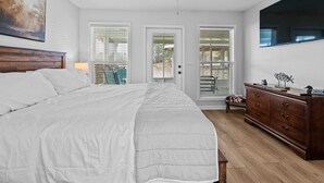 A bedroom with a large bed, a wooden dresser, a ceiling fan, and a TV mounted on the wall.