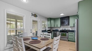 A modern kitchen with green cabinets, a stainless steel refrigerator, and a dining area with a wooden table and chairs.