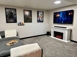 Un salón de cine en casa con televisor de pantalla plana, chimenea y tres carteles de películas en la pared.