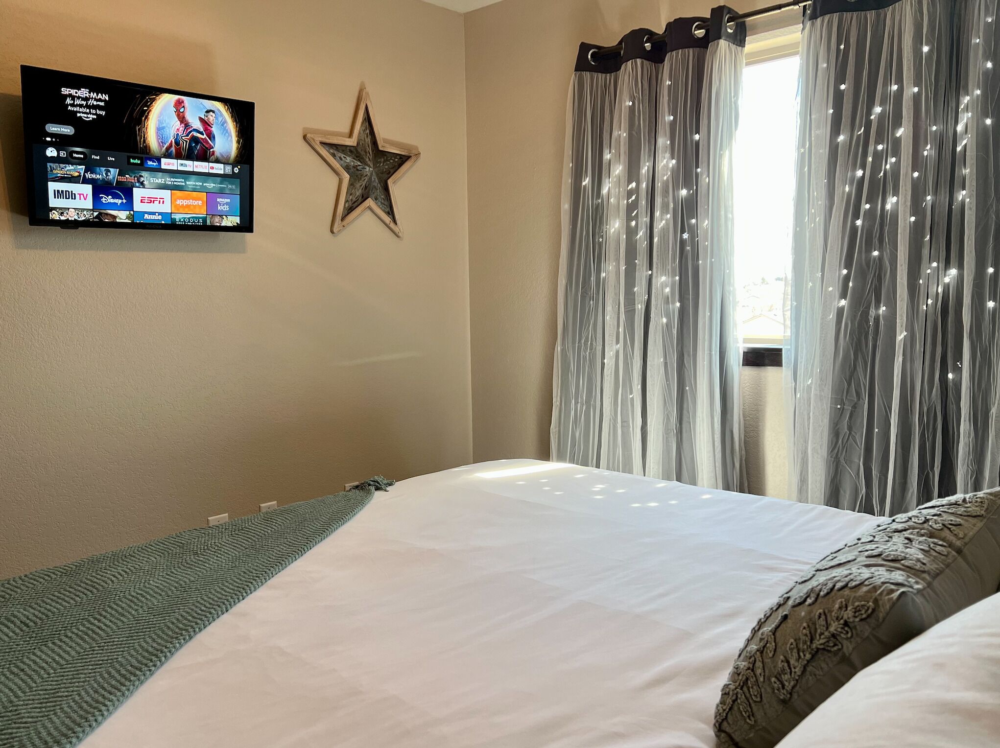 A hotel room with a bed, a star decoration, a television displaying a movie, and sheer curtains.