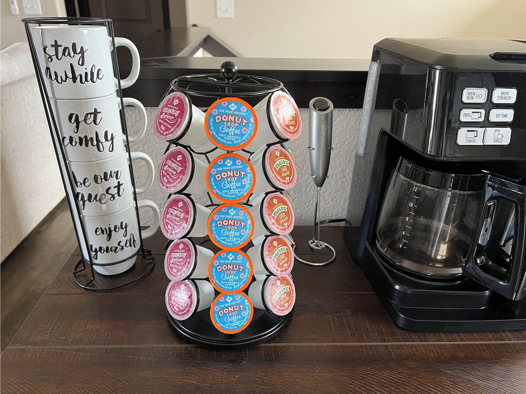 Une machine à café dotée d’un bac de récupération, une tasse ornée d’une citation motivante et une pile de dosettes de café.