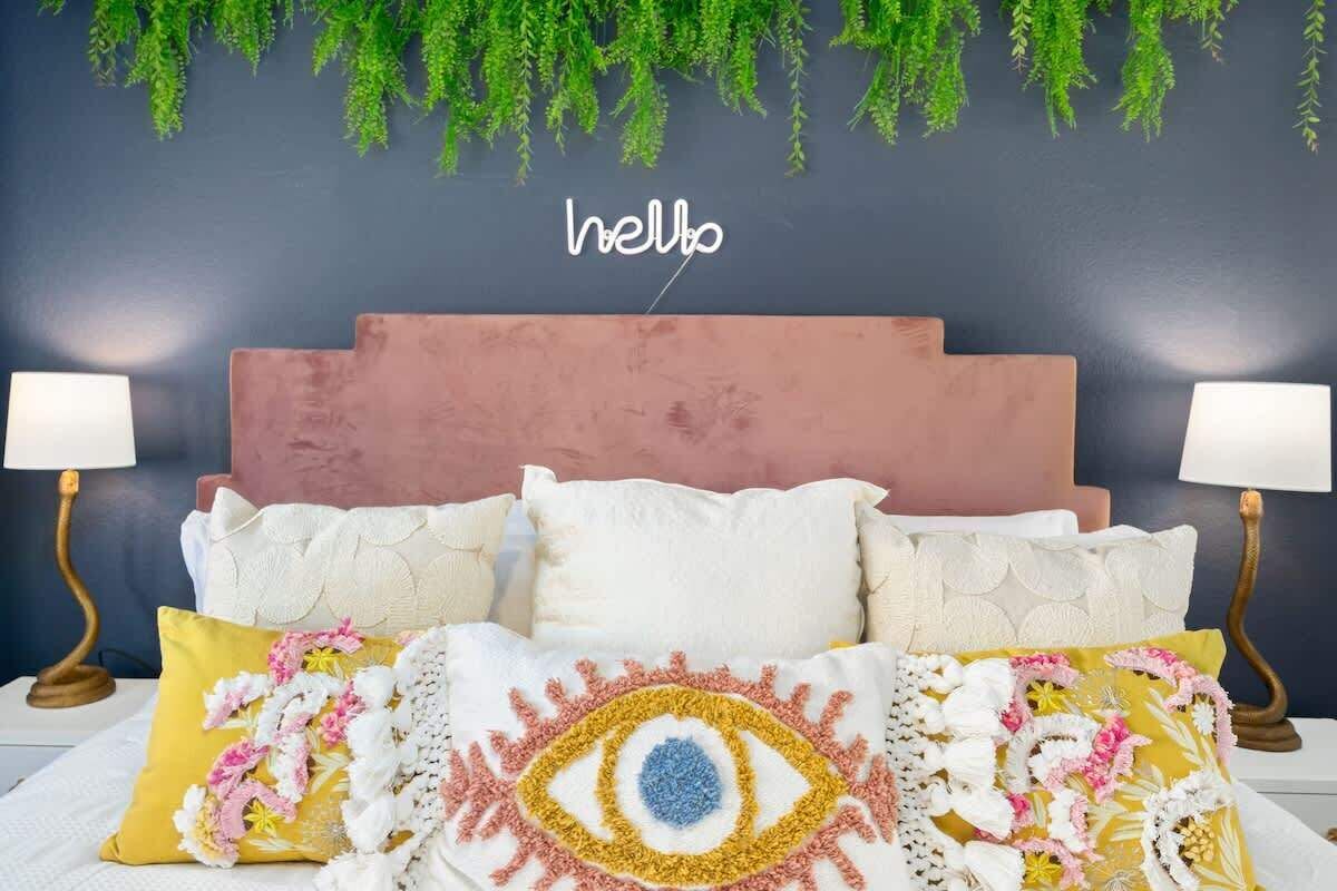 Un lit avec une tête de lit rose, des oreillers blancs et jaunes, et une couverture à motifs floraux.