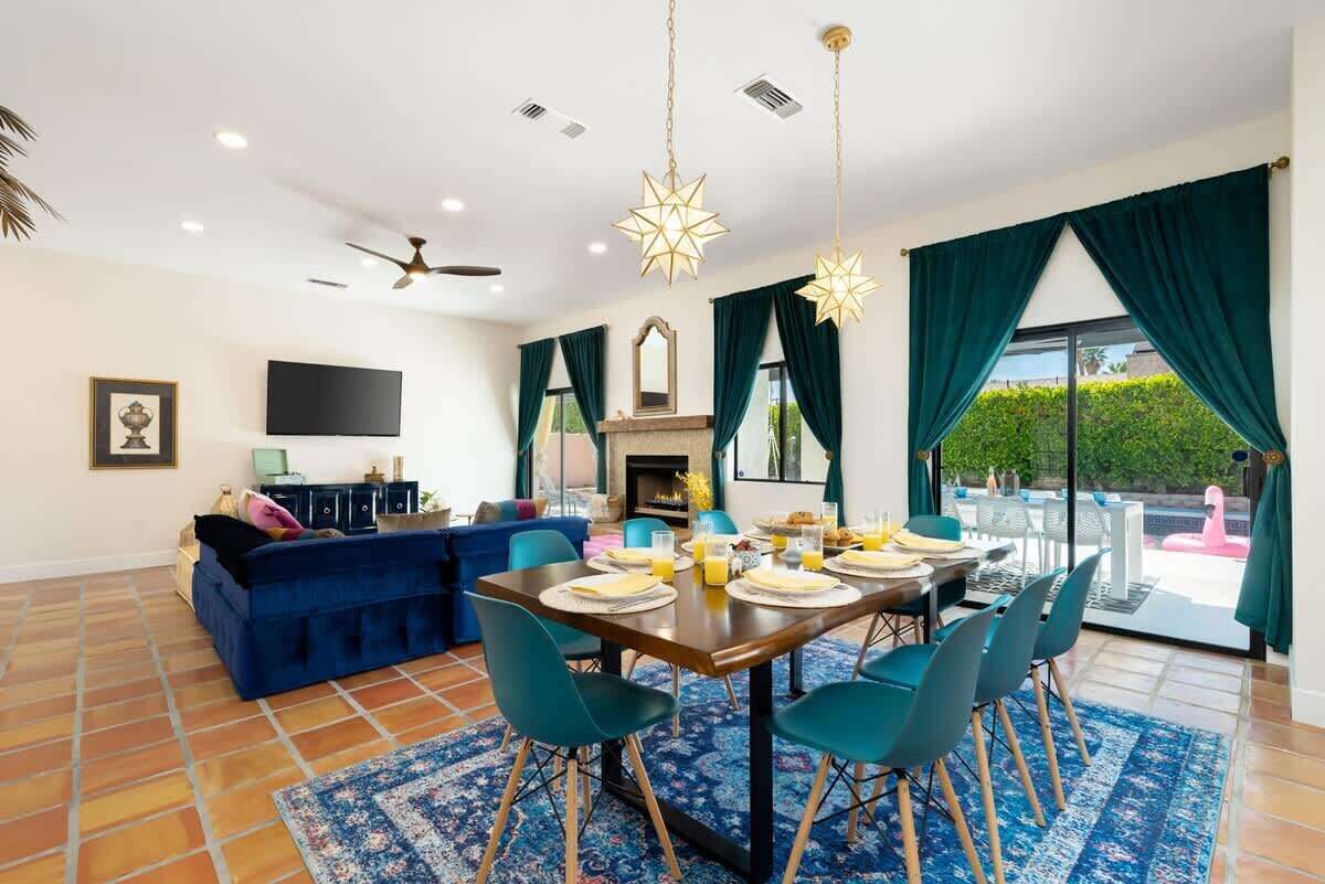 Un salón amplio con un sofá azul, una mesa de comedor preparada para cuatro personas y una chimenea.
