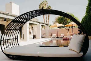 A poolside lounge area with a curved black metal chair, a small pool, and a white cushioned bench. - Moroccan Desert Oasis -Salt Pool + Spa + Game Room (Bermuda Dunes)