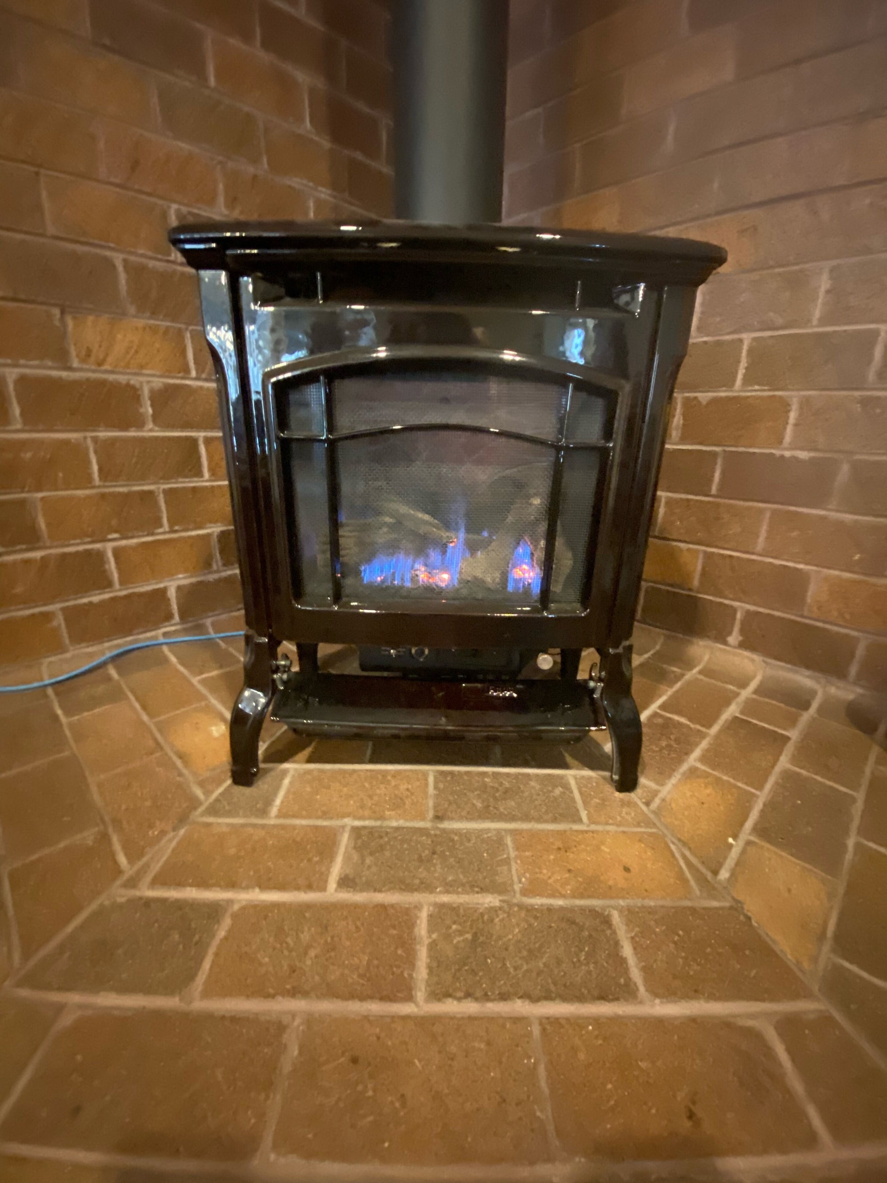 A wood-burning stove with a glass door, set against a brick wall.