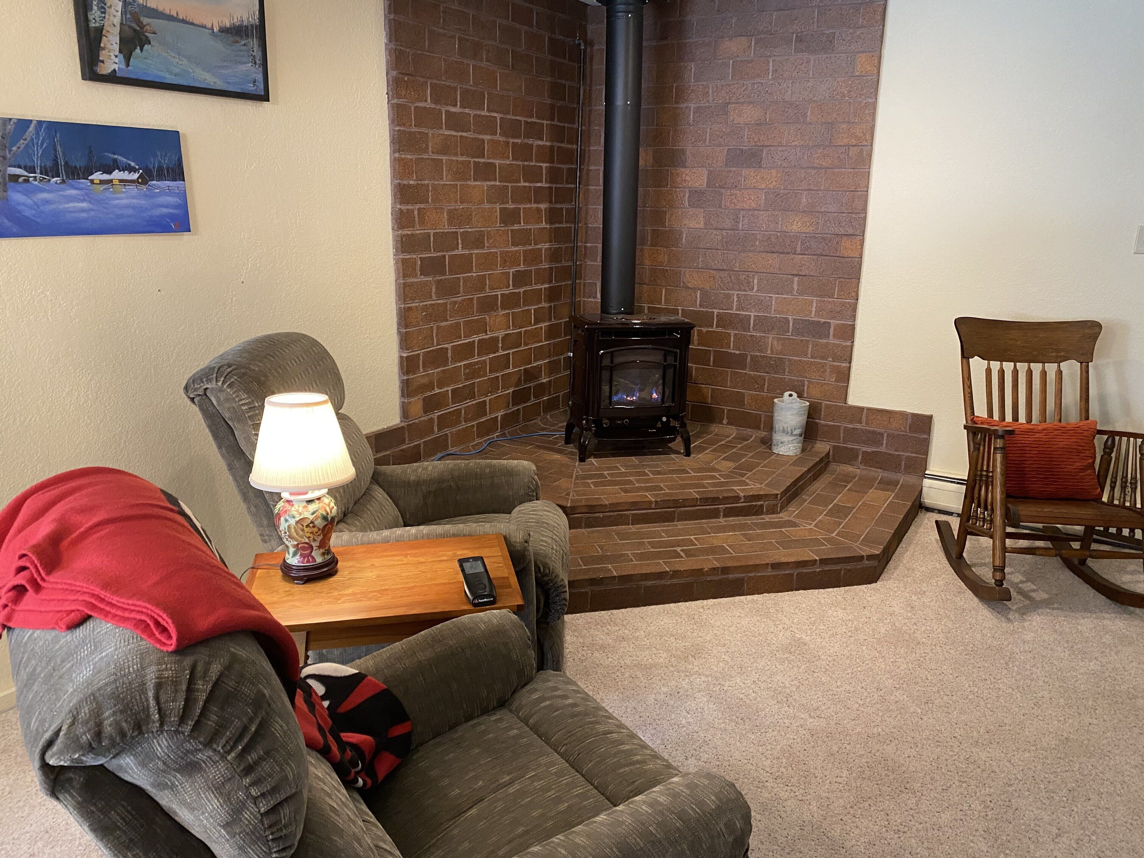 A cozy living room with a brick fireplace, a comfortable sofa, a wooden coffee table, and a rocking chair.