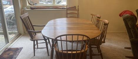 Un coin repas avec une table et des chaises en bois, une fenêtre donnant sur les arbres et un tableau encadré au mur.