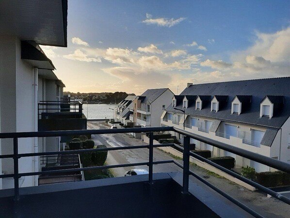 A residential area with houses along a waterfront, a balcony with a railing, and a clear sky. - Etel - 2-room apartment - 45m² - 3* (ETEL)