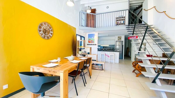 Un interior moderno con comedor, cocina y una escalera que sube a un altillo.