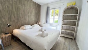 A modern bedroom with a large bed, a bedside lamp, a wicker basket, and a built-in shelving unit. - Charming villa in a quiet location with courtyard (LE BOIS PLAGE EN RE)
