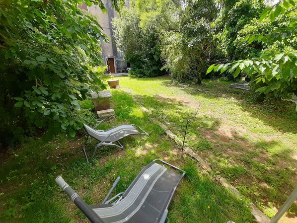 Un jardín con césped, un banco de piedra y una silla.