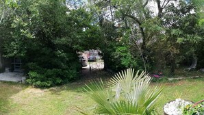 Um jardim com diversas plantas e árvores, uma estrutura de concreto e uma cadeira de metal.