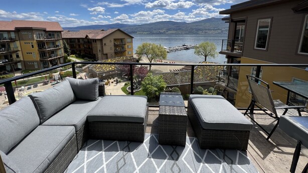 A balcony with a sofa and ottoman, overlooking a lake and buildings.