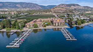 A waterfront hotel with multiple buildings, a marina with boats, and a backdrop of mountains and fields.