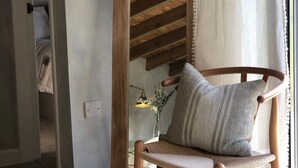 Ein spiegel, der einen Raum mit Holzboden, einem Stuhl mit Kissen und einem kleinen Tisch mit Lampe und Blumen reflektiert, eingefasst von Holz.