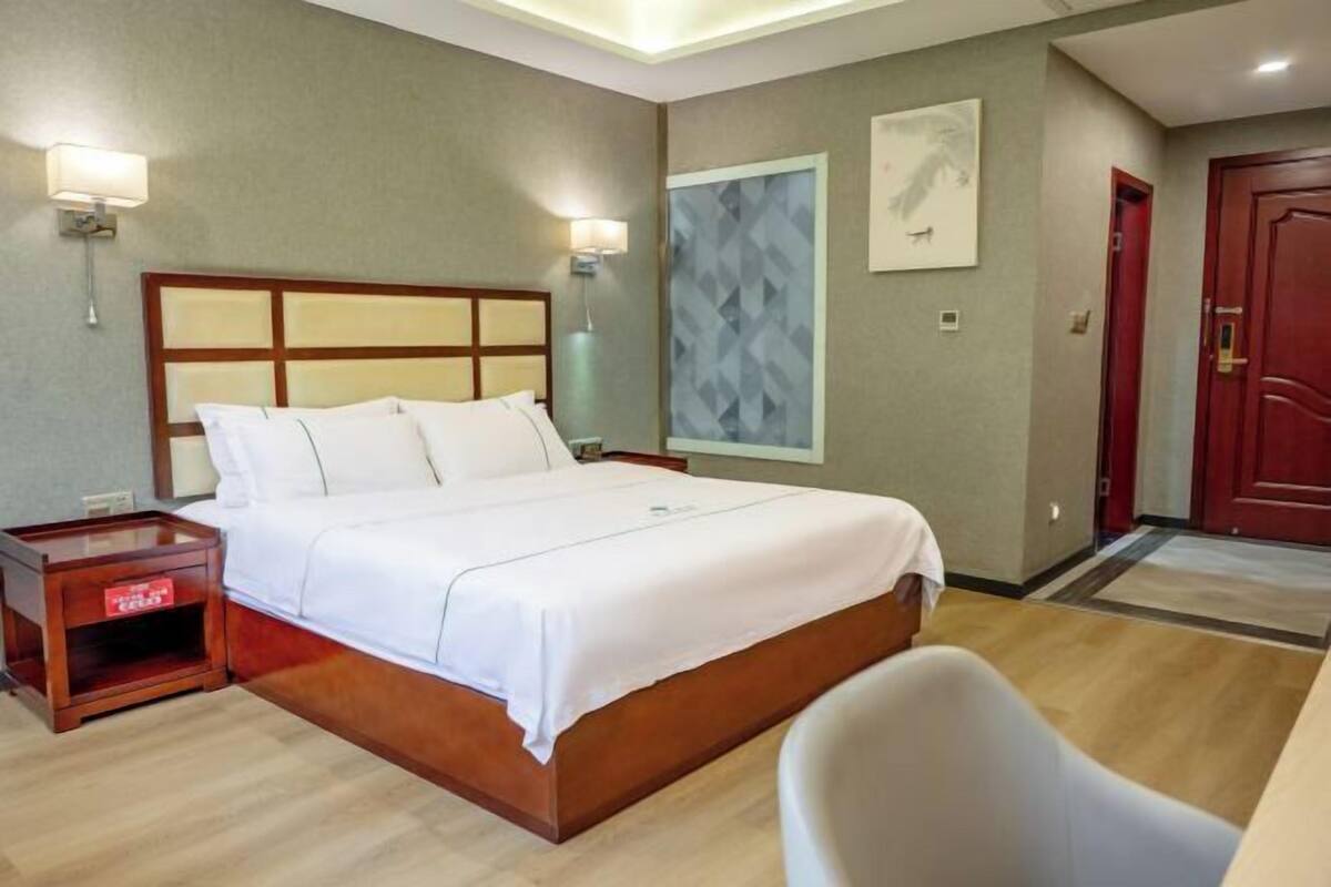 A hotel room with a bed, bedside tables, a chair, a wall-mounted artwork, and a door.