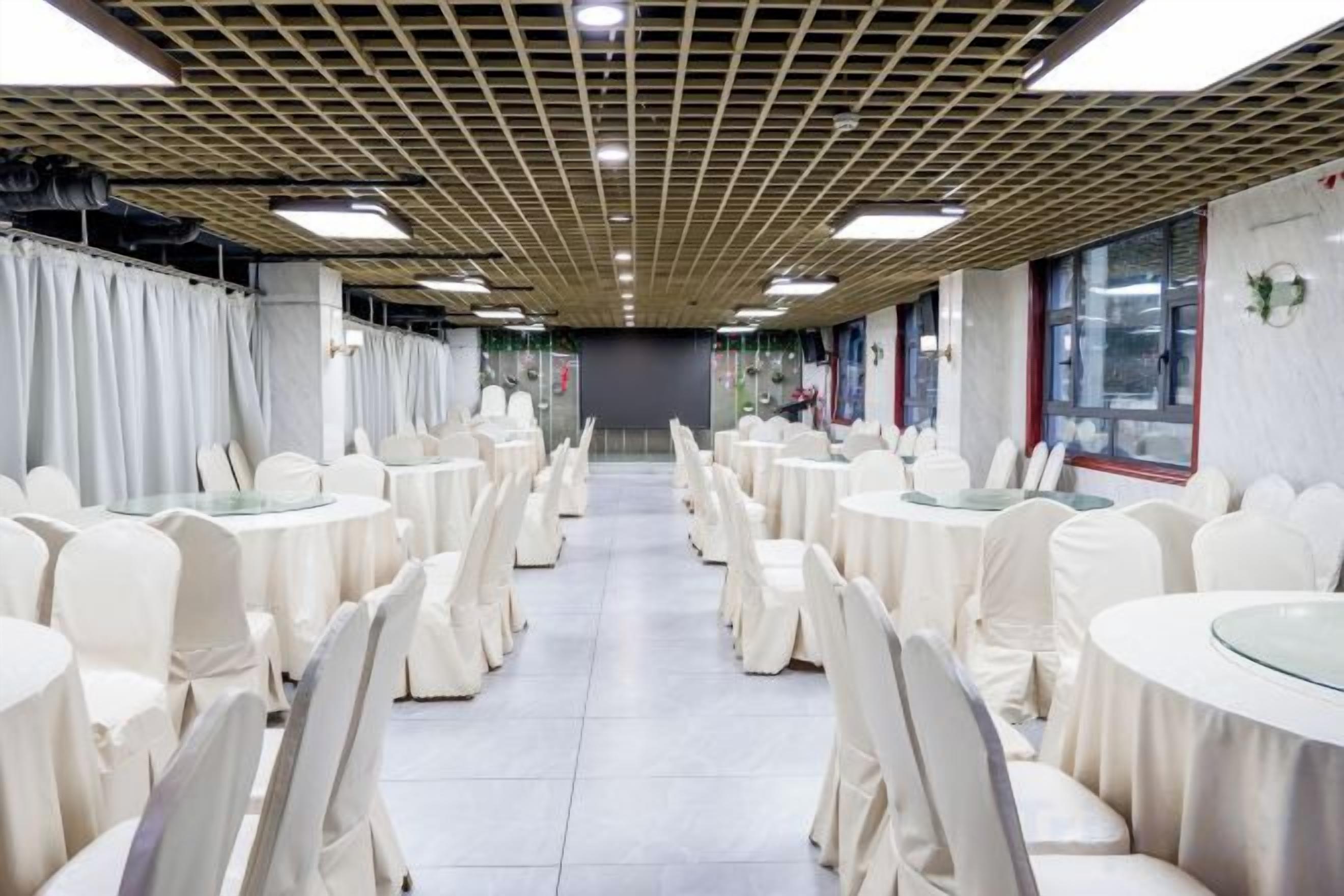 A banquet hall with round tables and chairs, a tiled floor, and a ceiling with a grid pattern.