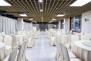 A banquet hall with round tables and chairs, a tiled floor, and a ceiling with a grid pattern. - Yajia Hotel (Kaiyang)