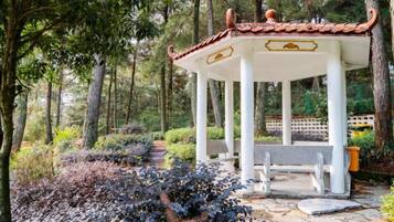 A gazebo with a tiled roof, surrounded by a garden with various plants and a stone pathway.