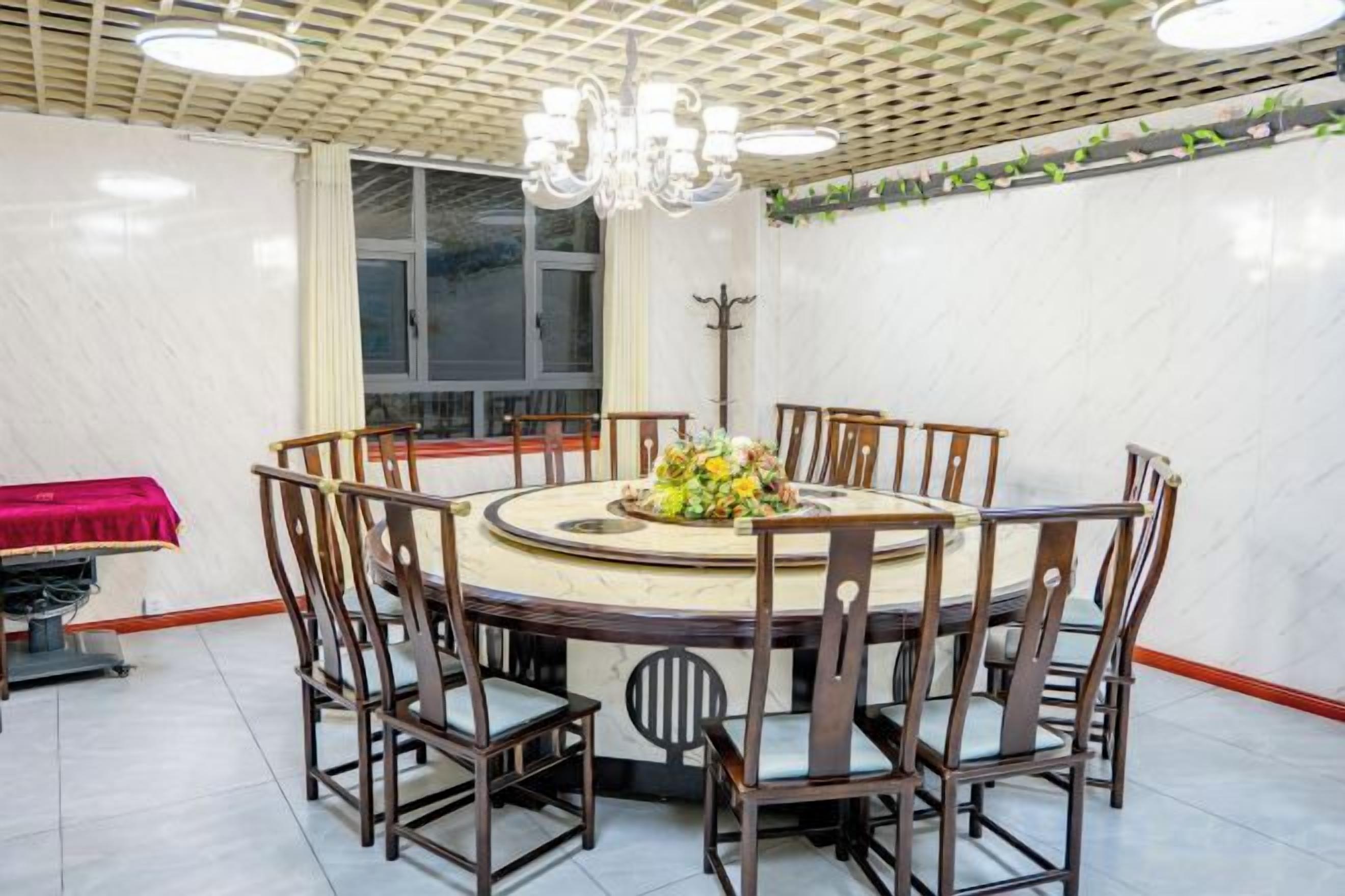 Un comedor con una mesa redonda rodeada de sillas, una araña y una ventana con cortinas.